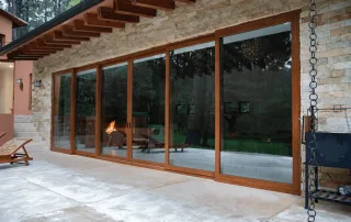 Sistema de puertas corredizas panorámicas en PVC de alta gama con acabado tipo madera, diseñado para ofrecer máximo aislamiento térmico y acústico en residencia de lujo con grandes ventanales.